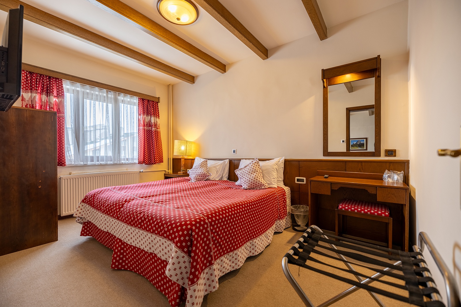 A Beceren bedroom interior with timber trim, a double bed and red patterned bedding beside a window